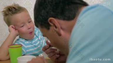 微笑的金发男孩与父亲说话用勺子吃饭和顽皮的近距离观察